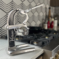 Metal citrus juicer with silver finish, black handle grip, and lever mechanism with collection cup.