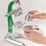 Manual citrus juicer with green and silver metal frame, lever handles, and two bowl attachments being held by hands.