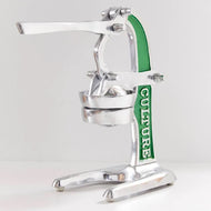 Stainless steel citrus juicer with green handle, lever arm, and collection cup on pedestal base.
