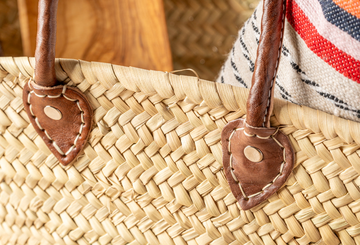Woven straw basket with brown leather handles and striped fabric trim in red, white, and navy.