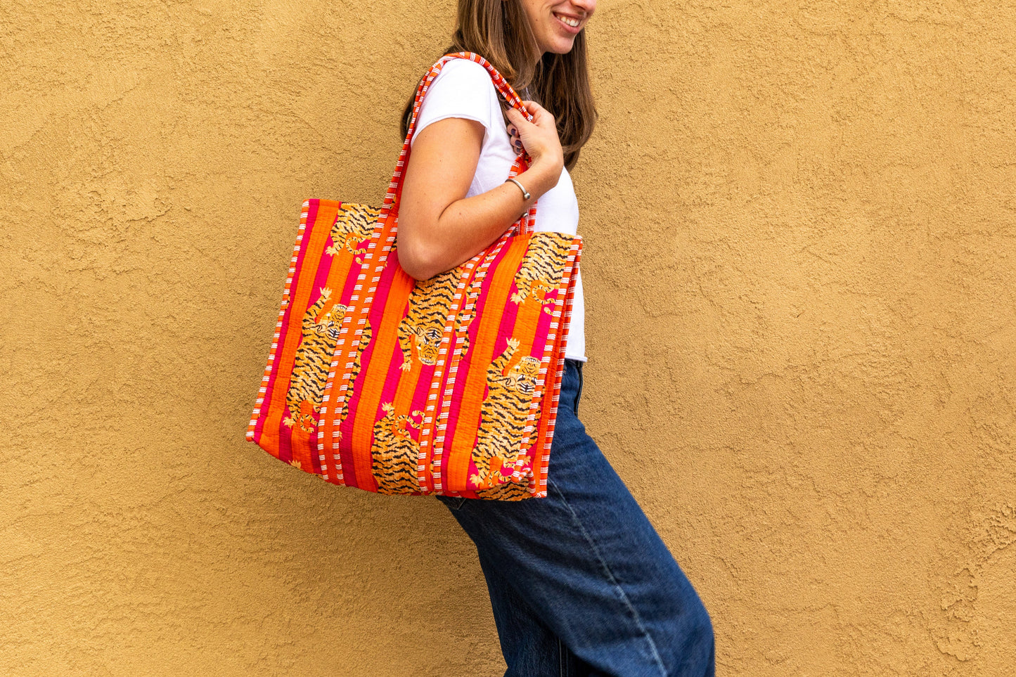Red and gold quilted tote bag with cat face design, worn over shoulder by model against yellow background.