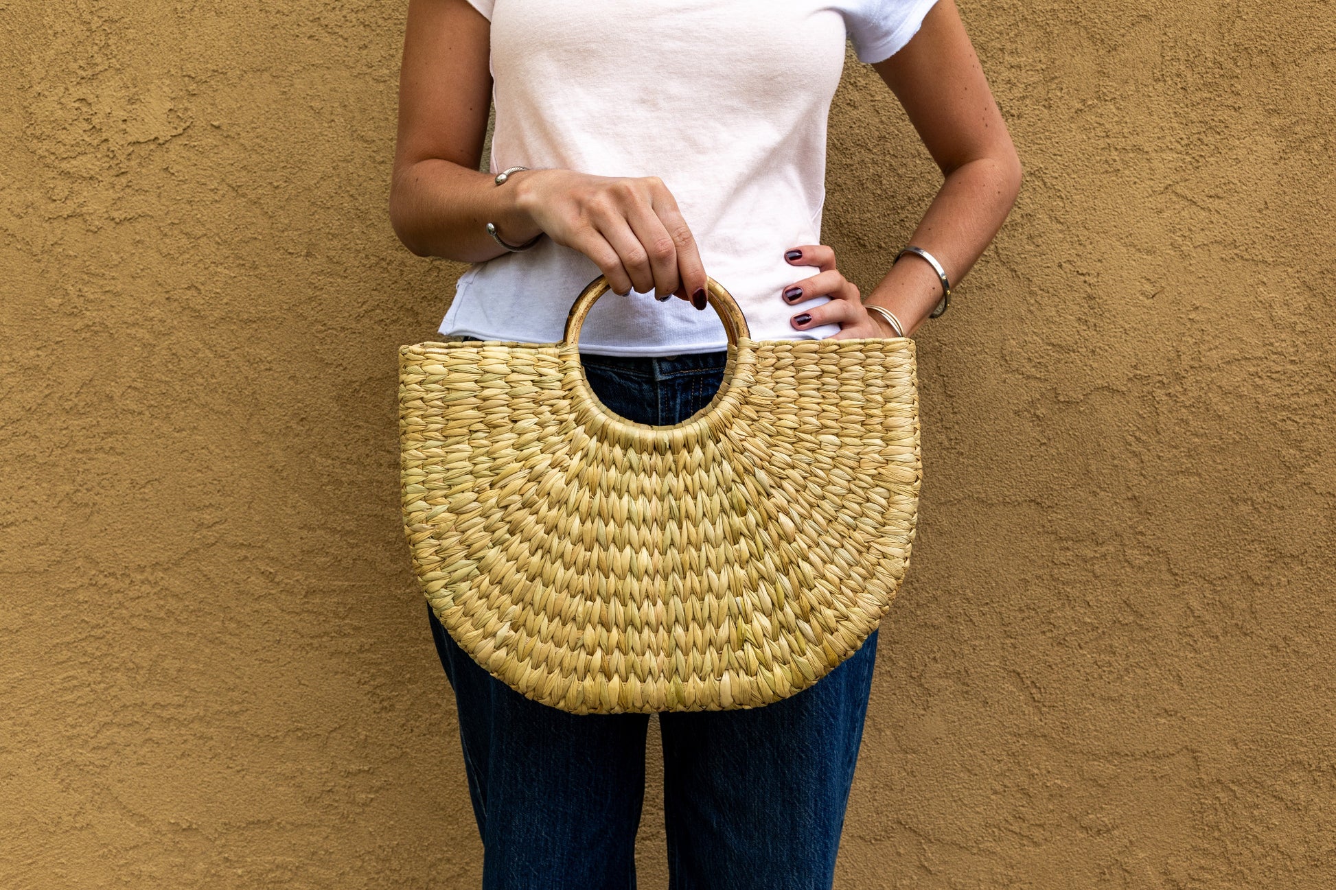 Woven straw tote with circular handle in natural tan and navy color blocking, held at waist level.