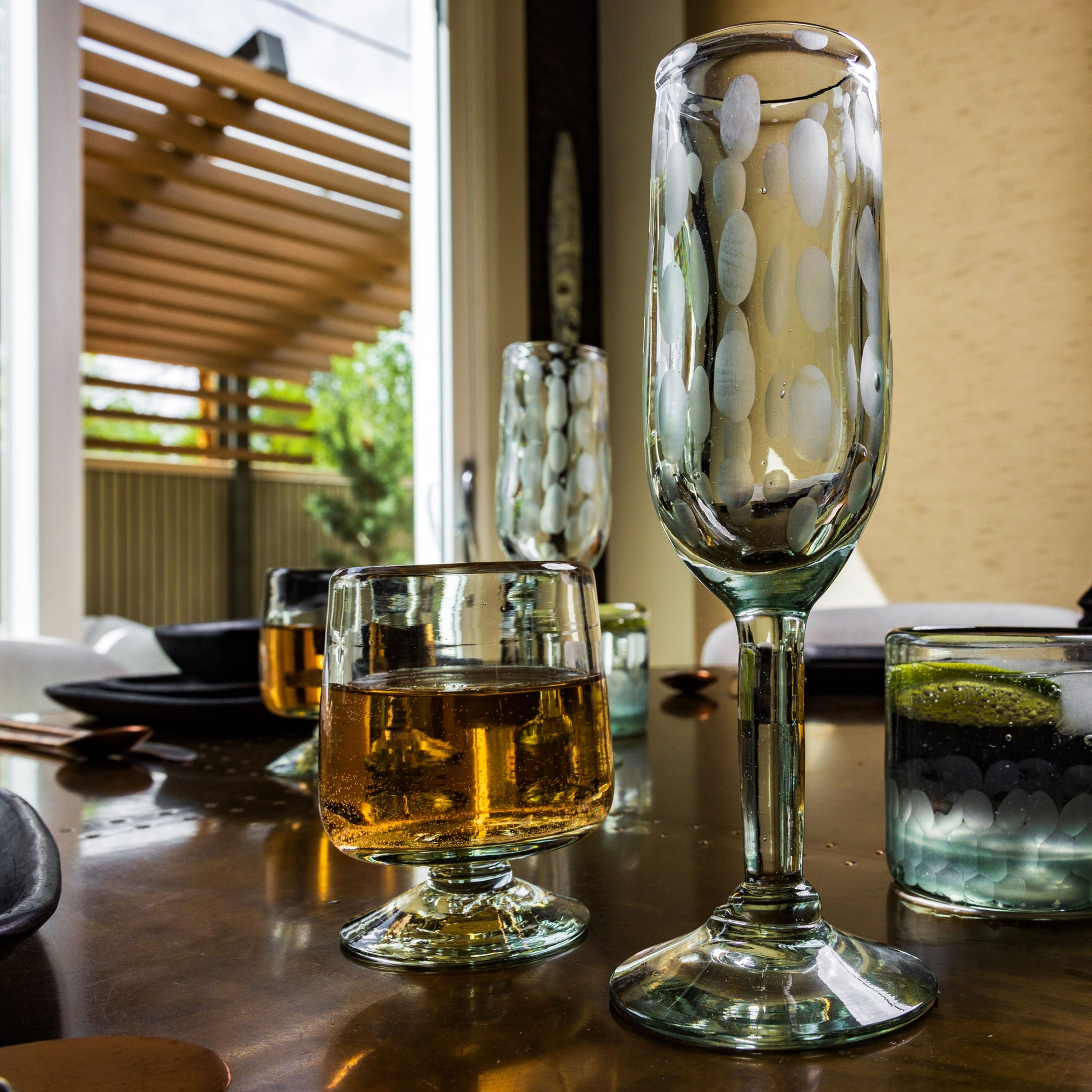Two clear glass champagne flutes with etched oval patterns, one filled with amber liquid, displayed on a dining table.