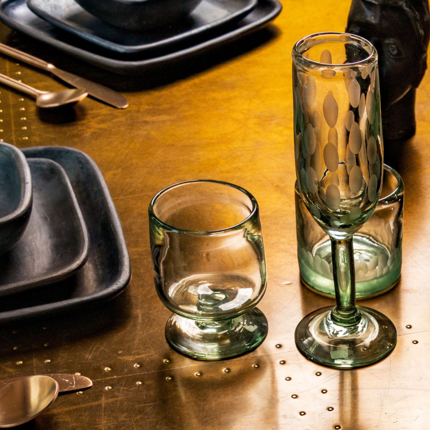 Two clear glass champagne flutes with etched leaf patterns and green-tinted stems on a gold table.