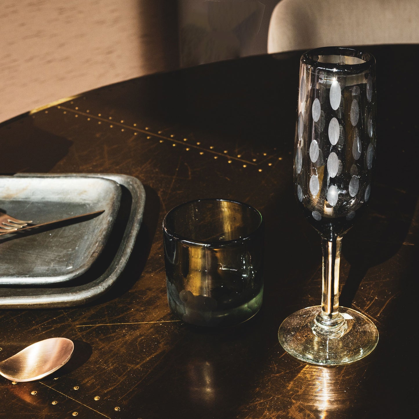 Two clear champagne flutes with etched dot pattern, one filled with liquid, displayed on dark table with place setting.