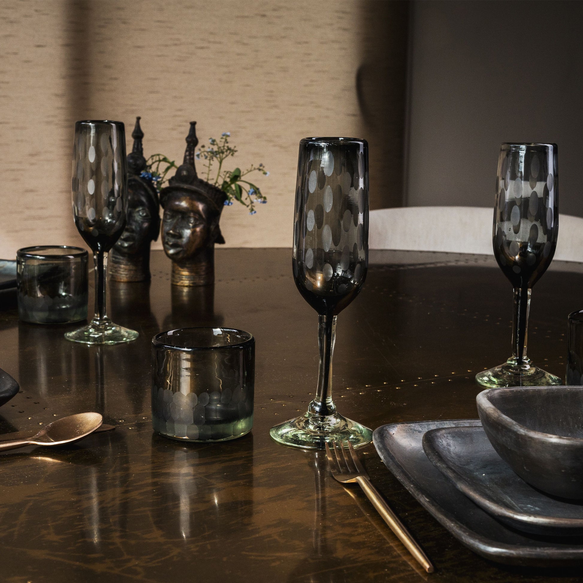 Two clear champagne flutes with white etched dot pattern on dark table setting.