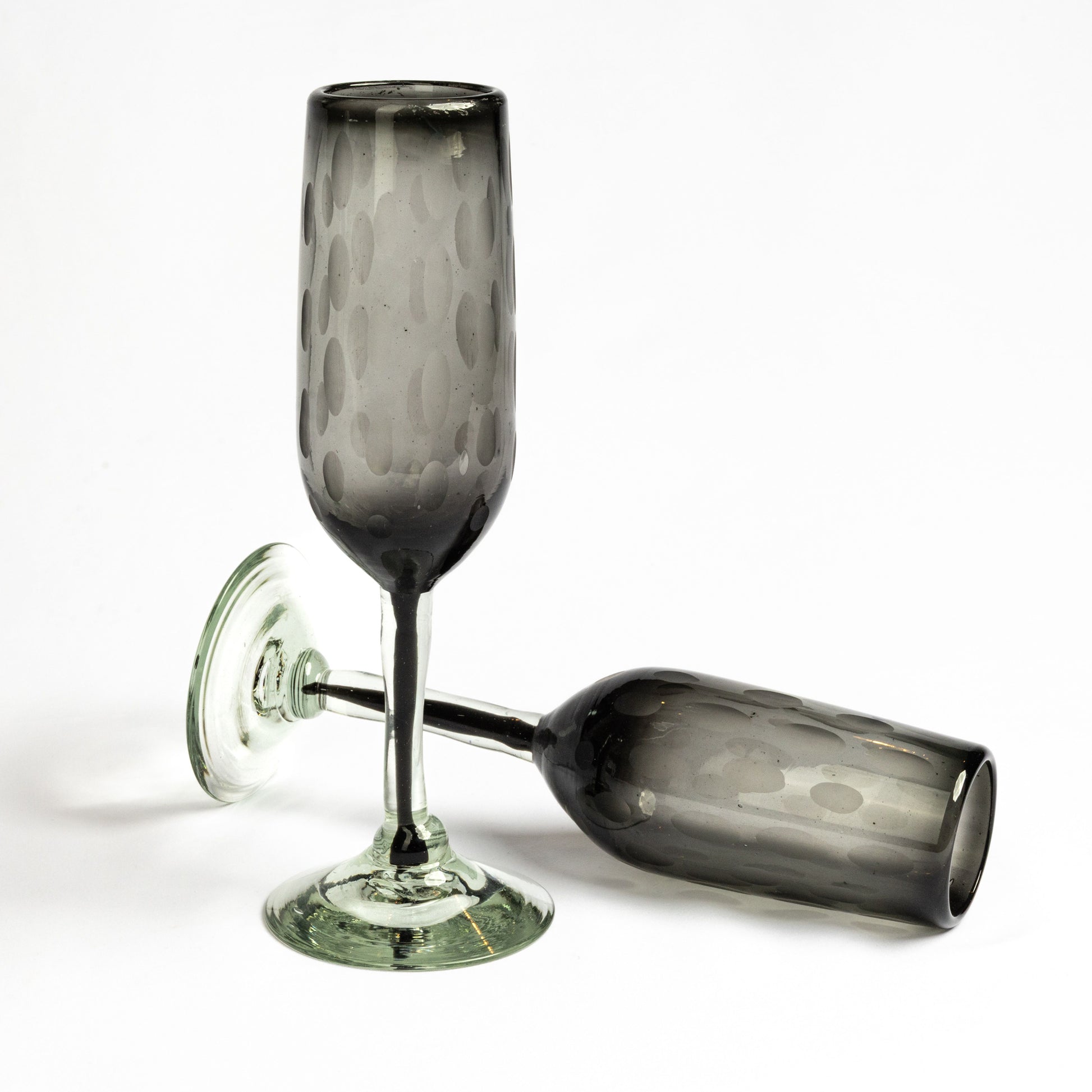 Two smoky gray handblown champagne flutes with etched oval patterns and green-tinted bases.