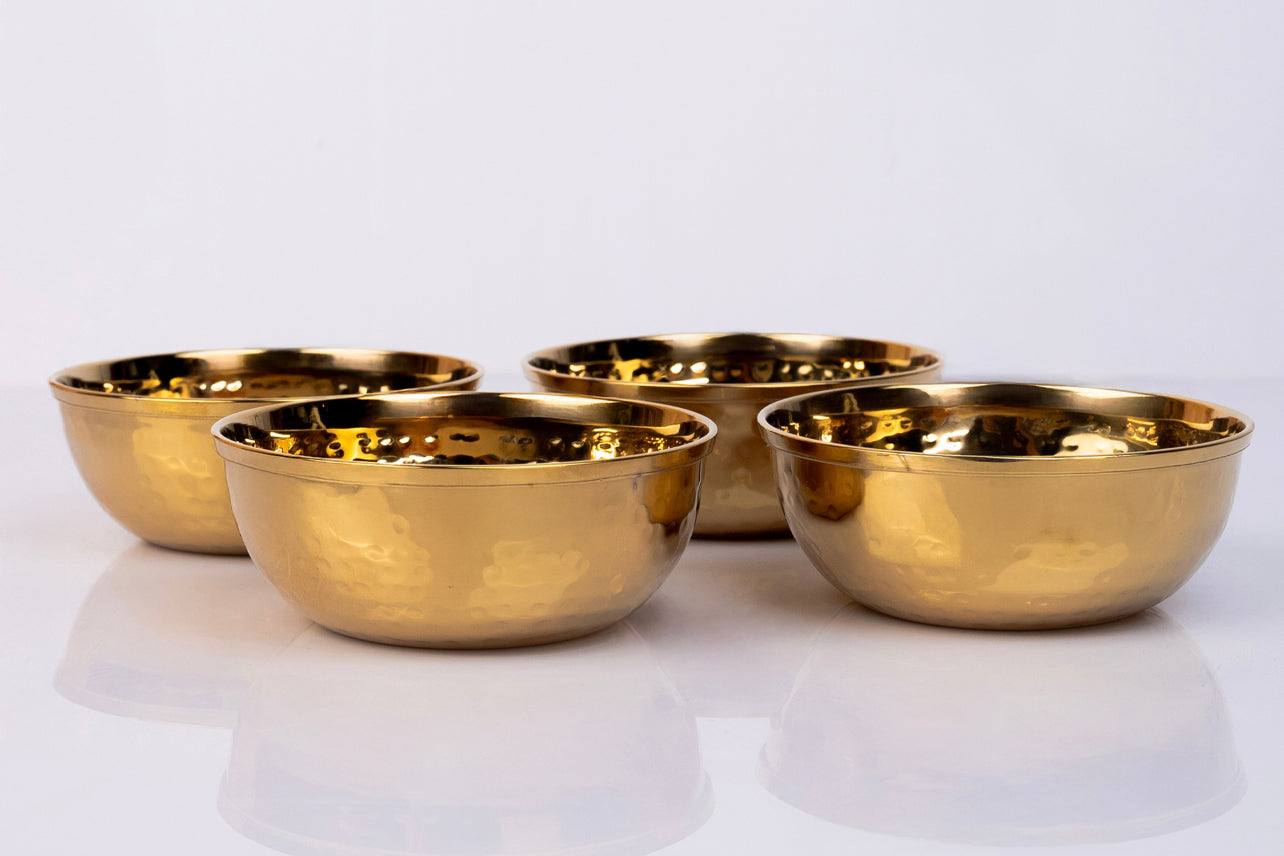 Four gold-colored hammered stainless steel bowls with curved sides arranged on a white surface.