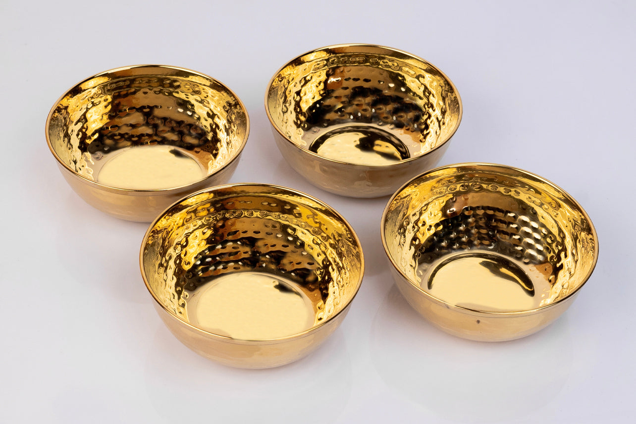 Four gold-toned stainless steel bowls with hammered texture finish arranged on white surface.