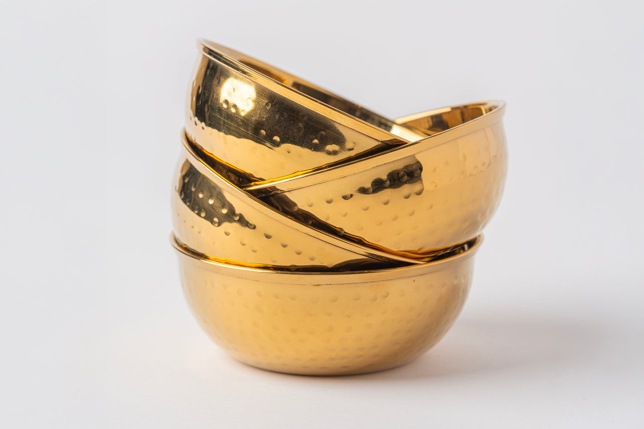 Four gold-toned stainless steel bowls with hammered surface texture stacked together.