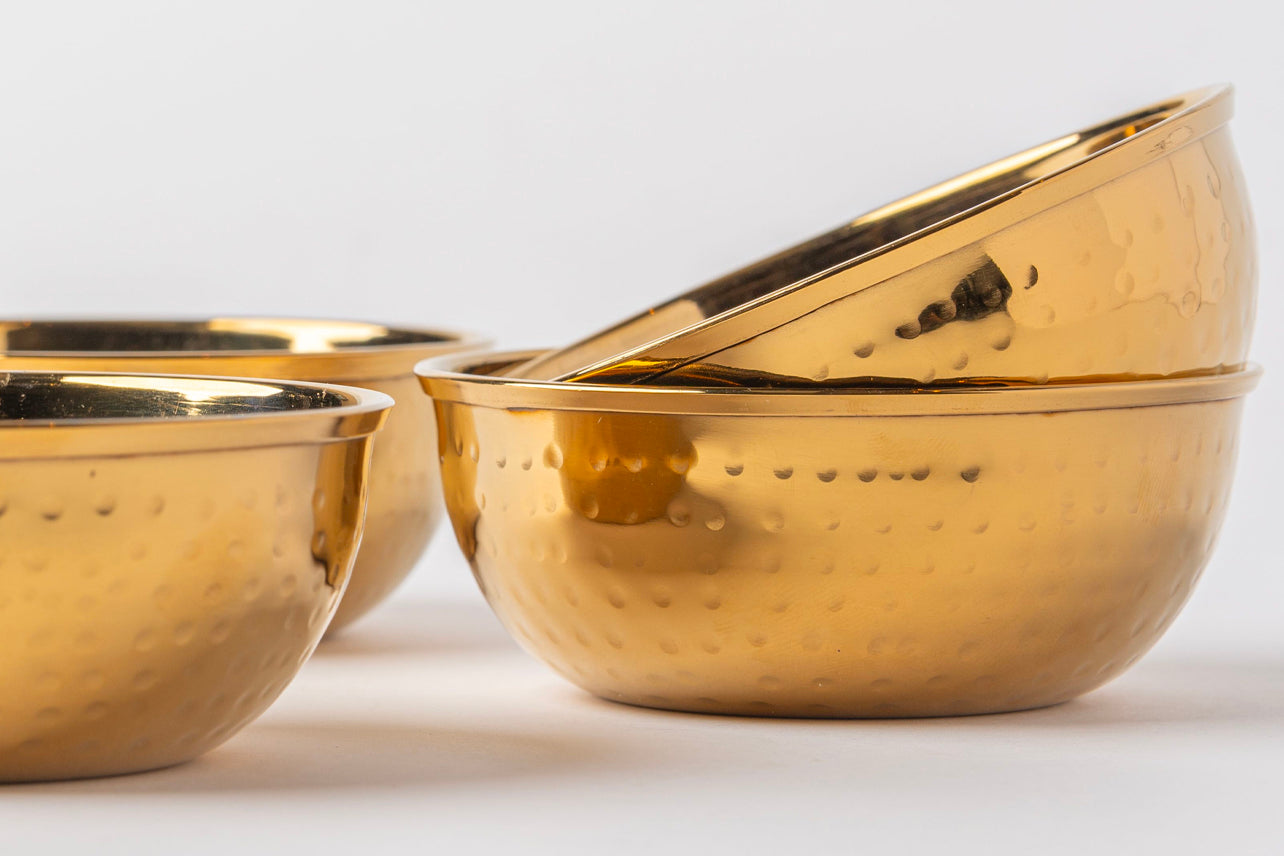 Set of four gold-toned stainless steel bowls with hammered surface texture and rim handles.