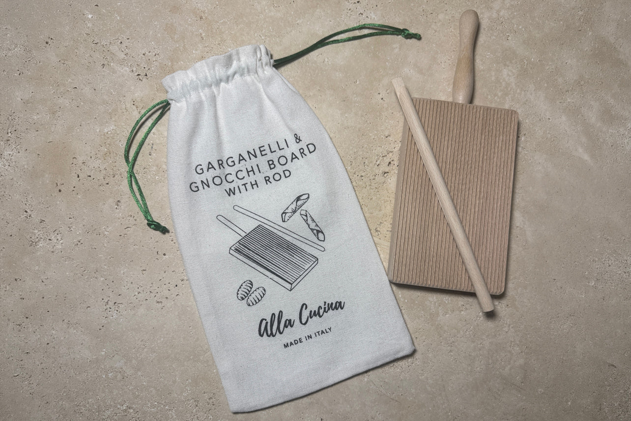Wooden gnocchi and garganelli board with rolling pin and white cotton drawstring storage bag on concrete surface.