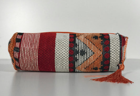 Barrel-shaped cosmetic bag with woven geometric pattern in red, cream, orange, and black with tassel closure.
